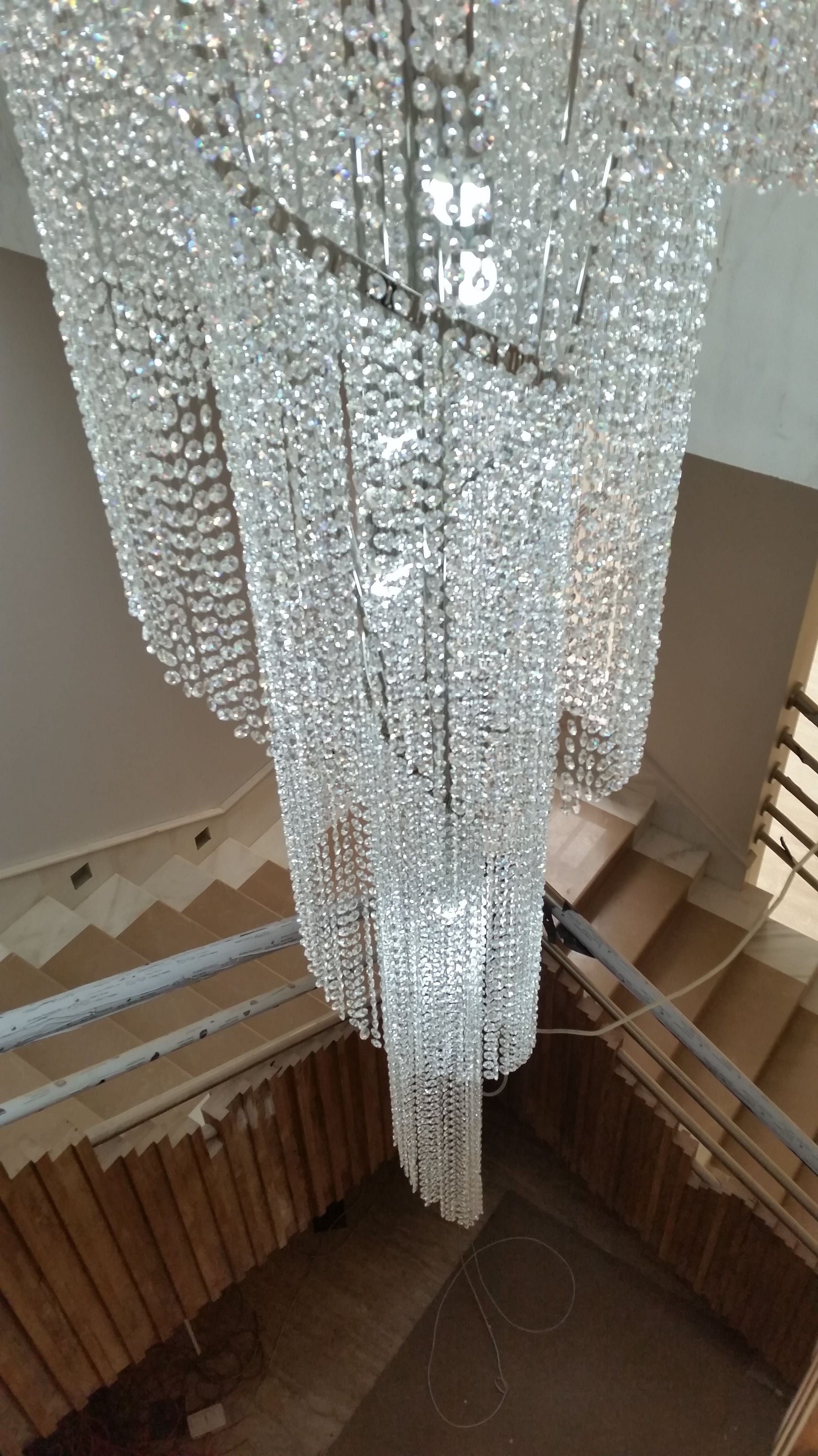 Tall crystal Twister-style staircase chandelier with matching crystal waterfall wall lights, installed in a client's foyer