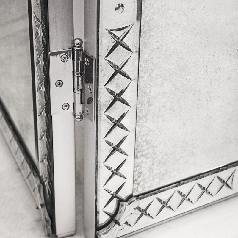 Close-up of a decorative mirror door with intricate patterns and a hinge.