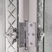 Close-up of a metallic door hinge on a decorative mirror door with engraved patterns.